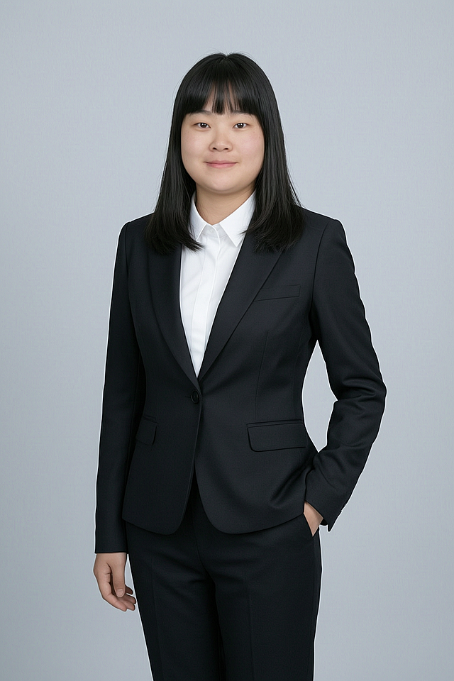 基于原图人物生成商务形象照，人物身穿黑色亚面精纺面料西装外套、黑色亚面精纺面料西裤，内搭白色衬衫，背景为简约冷调浅灰色纯色背景，背景光线均匀柔和，呈现均匀柔和质感，极简干净，强化色彩对比的高级感。采用标准焦段50mm，F/4光圈，平视视角，镜头与人物视线齐平，人物占画面70%，人物居中构图，位于画面中心为视觉聚焦点，入境范围为头部及以下至臀部下方10cm，半身像构图，人物呈正面单手插兜姿态，左手插在西装裤侧缝口袋仅露出手腕部分，右臂自然垂落，肢体自然，自信从容