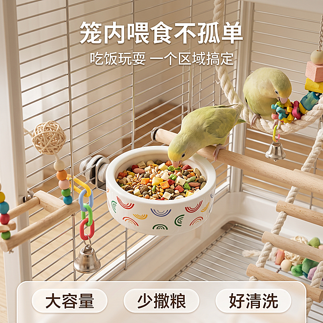 第 2 屏｜笼内玩具陪伴场景主图，960×960px 正方形电商主图，8K 超清、300DPI、sRGB 色域，真实宠物用品生活场景摄影风格，柔和窗边自然光，浅米白、浅原木色、淡绿色为主色，画面干净温馨，无生硬阴影。画面核心是一款白色鹦鹉磁吸陶瓷食碗，参考用户上传产品图：圆润浅口陶瓷碗、厚实碗壁、亮面白釉、外壁彩色弧形图案、碗内鹦鹉花卉图案完整清晰，产品安装在鸟笼内壁上，金属磁吸固定件可见，突出安装稳固和笼内使用场景。食碗内盛放鹦鹉粮食、种子、滋养丸和少量果蔬颗粒，粮食饱满但不溢出。画面中一只鹦鹉站在旁边木质站杆上低头进食，另一只鹦鹉可在附近玩具上轻微互动，形成热闹但不拥挤的笼内生活感。产品周围点缀鹦鹉玩具组合：木质秋千、彩色吊链、藤编球、木珠串、铃铛、云梯、小型站台，颜色以原木色、奶白色、浅绿色、少量暖黄色为主，避免过度鲜艳杂乱。构图采用中心聚焦，食碗位于画面下半部中央偏前，是最大视觉主体，鹦鹉位于食碗上方或旁边，玩具围绕食碗形成笼内活动区，背景简洁明亮，突出这款食碗是鹦鹉日常吃饭、玩耍、陪伴的核心用品。画面文字避开产品，顶部居中主标题为 “笼内喂食不孤单”，副标题为 “吃饭玩耍 一个区域搞定”，底部圆角卖点栏为 “大容量｜少撒粮｜好清洗”。字体简洁清晰，排版不遮挡食碗。反向提示词：玩具堆砌过满、食碗被遮挡、鹦鹉比例异常、鸟笼背景过乱、塑料感强、颜色廉价、文字压在产品上、产品结构错误、碗口图案变形、画面噪点、卡通插画感、过度广告感、水印二维码。