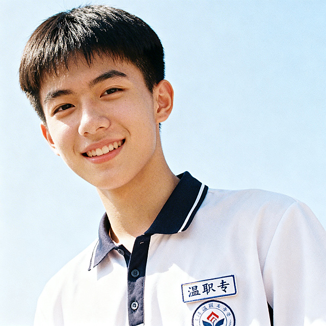 温职专的帅气男学生，面容清爽干净，发型整齐符合校园仪容仪表规范，胸前佩戴着温职专的校徽，穿着整洁的校服，神态阳光开朗，校园青春风格，画面清晰自然