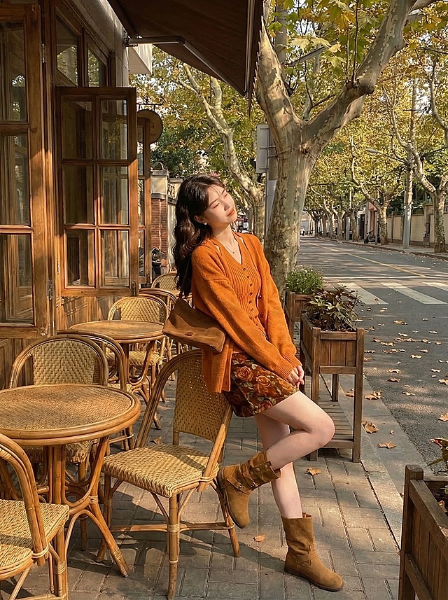 保留这套焦糖色秋日穿搭：暖橘色针织开衫+挂脖针织吊带+棕色玫瑰碎花短半身裙+棕色短靴，斜挎棕色包包，在复古咖啡馆梧桐露台，午后暖金色阳光斑驳，着重凸显服饰细节和面料质感，慵懒松弛秋日氛围感，抖音带货风格，模特姿态自然