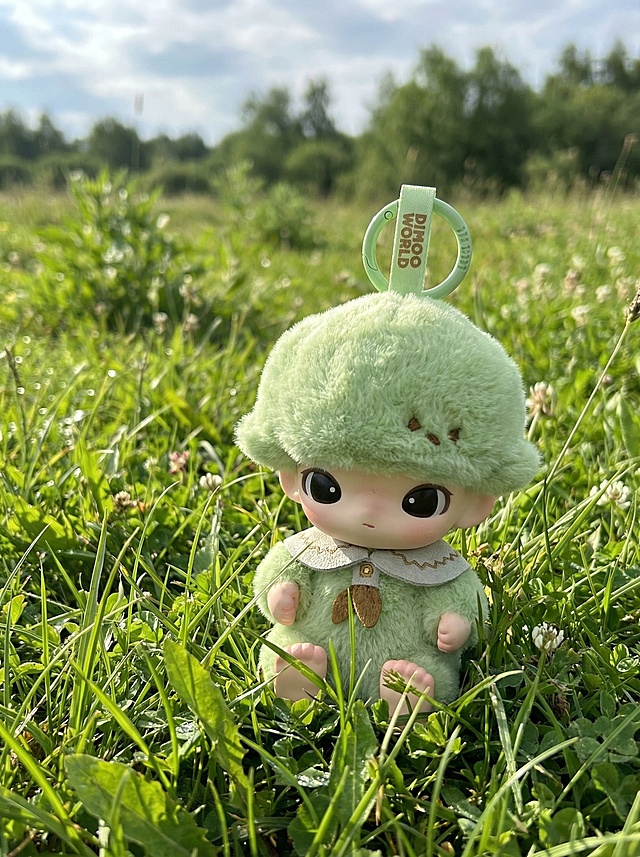 保留图片中的绿色玩偶主体，将背景替换为真实的绿色自然草地，玩偶位置可合理调整，画面风格写实自然
