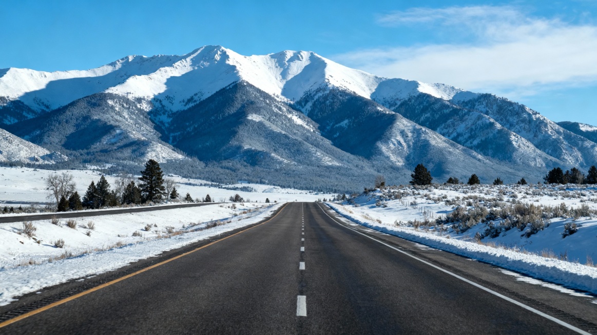 帮我生成一张背景大图，要求背景远景为雪山，中间为一个单向四车道，车道两侧风景被雪覆盖，车道内没有积雪预览效果