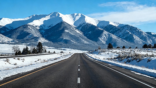 帮我生成一张背景大图，要求背景远景为雪山，中间为一个单向四车道，车道两侧风景被雪覆盖，车道内没有积雪
