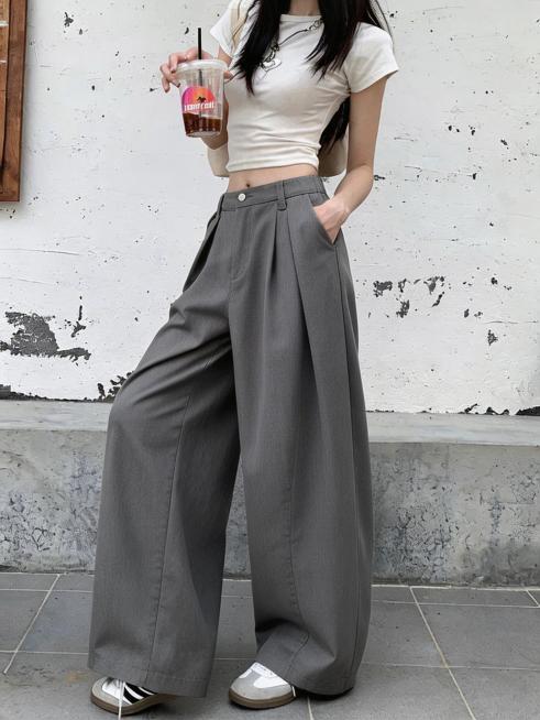 将图二的灰色阔腿西装裤替换到图一模特的下半身，保持图一模特的姿势、白色短袖上衣、手中的饮品、背景墙面地面、鞋子都完全不变，裤子贴合模特身材，光影自然，与整体画面协调统一预览效果
