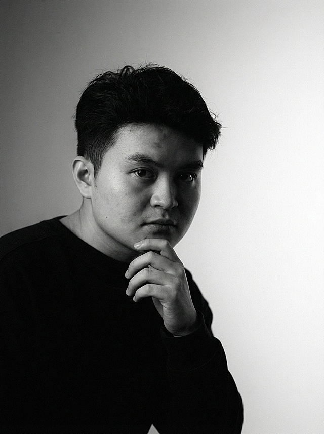 将上传的照片转换成高分辨率的黑白肖像艺术作品，采用编辑类和艺术摄影风格。背景呈现柔和渐变效果，从中灰过渡到近乎纯白，营造出层次感与寂静氛围。细腻的胶片颗粒质感为画面增添了一种可触摸的、模拟摄影般的柔和质地，让人联想到经典的黑白摄影。
画面中的人物，模糊却惊艳的面容从阴影中隐约浮现，并非传统的摆拍，而像是被捕捉于思索或呼吸之间的瞬间。他的脸部因为光线的轮廓，唤起神秘、亲密与优雅之感。他的五官精致而深刻，散发出忧郁与诗意之美，却不显矫饰。
一束温柔的定向光，柔和地漫射开来，轻抚他的面颊曲线，或在眼中闪现光点—一这是画面的情感核心。其余部分以大量负空间占据，刻意保持简洁，使画面自由呼吸。画面中没有文字、没有标志—只有光影与情绪交织。整体氛围抽象却深具人性，仿佛一瞥即逝的目光，或半梦半醒间的记忆：亲密、永恒、令人怅然的美。
小要求没有实物的背景，每张照片换不同的动作。