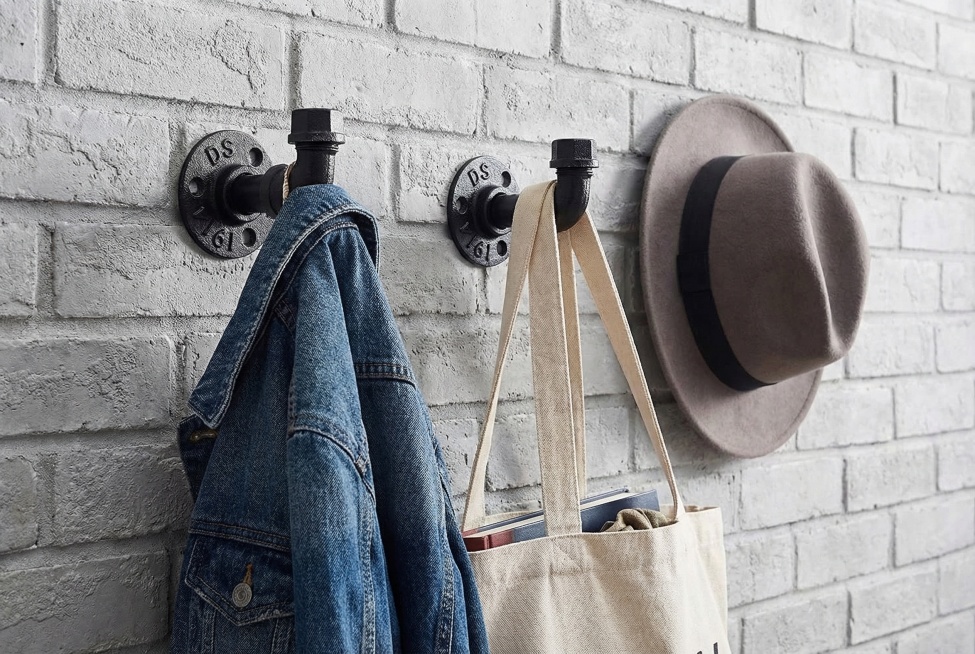 亚马逊A+详情图，工业风复古墙面，黑色铸铁水管支架安装在浅灰色砖墙面上，支架横杆上挂着牛仔外套、帆布包、帽子等日常衣物配饰，光线明亮柔和，突出产品承重能力与实用场景，画面简洁高级，符合电商详情页风格预览效果