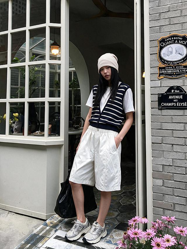 保持人物、服装、背景、光影、构图完全不变，仅修改模特的姿势：一只手插在裤子口袋里，另一只手自然提着黑色托特包，身体微微侧转倚靠在门框上，头部正对镜头，姿态慵懒随性。其余画面元素保持原样，真实皮肤肌理，衣物面料纹理清晰，高清写实，清冷低饱和韩系街拍风格。