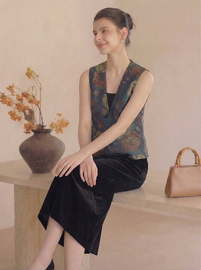 保持人物主体不变，保持移除口袋后的深蓝色花卉提花马甲和黑色丝绒半身裙服饰不变，生成一个自然放松的全新姿态，保留原米白墙面、陶罐花艺场景，维持暖调柔和光影和真实质感