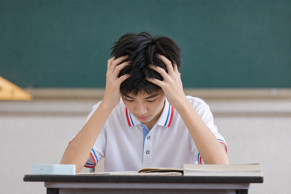 参考原图的教室课堂场景和人物抱头学习的动作构图，更换人物为全新的14岁左右中学生，保持自然写实的校园摄影风格，整体场景和服装风格不变预览效果