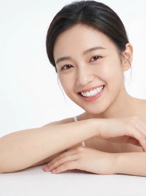 笑容灿烂的年轻东亚女性模特，露出洁白整齐的牙齿，神态清新自信，相貌与参考图不同，胳膊自然放在桌面上，画面中没有任何产品、文字，背景为纯白色，写实人像摄影风格，光线柔和自然，画质清晰预览效果