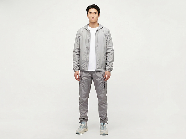 根据参考图服装样式重构，生成一张干净简约风格的男士浅灰色运动套装商品展示图，保持浅灰色连帽外套+同色系工装束脚运动裤+内搭白色T恤的服装结构不变，保持产品主体物理结构不变，纯色干净背景，商业高调摄影，柔和漫射光，低对比度，画面整体明亮干净通透，东亚模特自然站立，保持服装版型和整体款式不变，保留服装的褶皱和质感，全身展示，三分法构图，30%留白。负向提示词：西方面孔、金发、深眼窝、雀斑、死黑阴影、硬光、高对比度、比例失调、摄影灯、柔光箱、水印、文字、昏暗光线、畸变透视