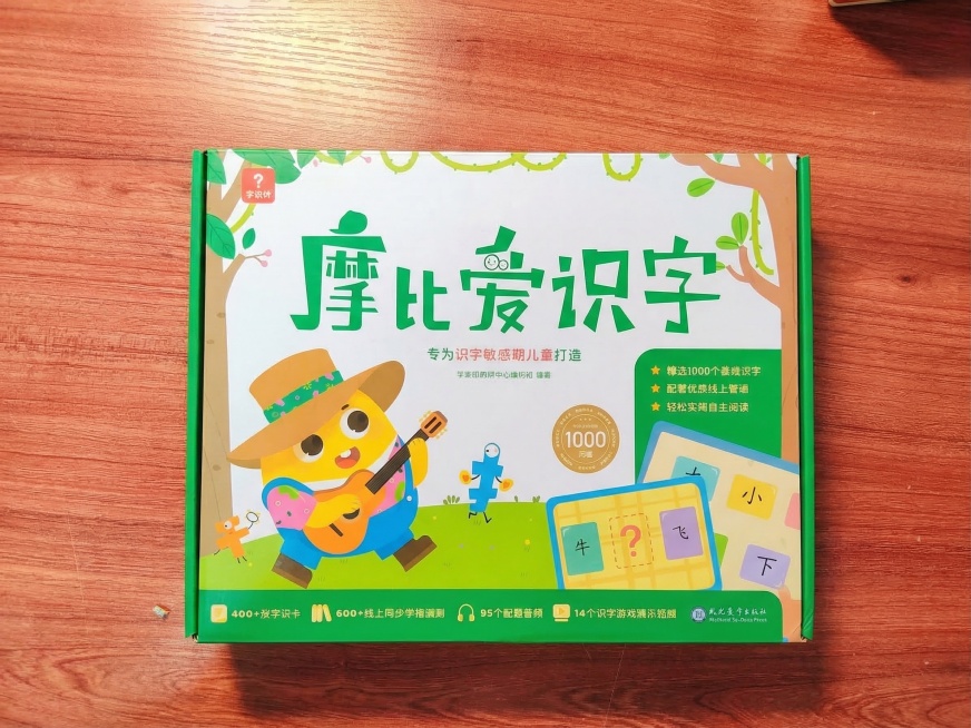 将图一的摩比爱识字礼盒自然融入图二的红棕色木质桌面背景。
1. **光影匹配**：背景光源来自左上方，在书本右下方生成符合物理规律的投影，阴影近实远虚，保持主体盒子原有外形和高宽比不变。
2. **文预览效果
