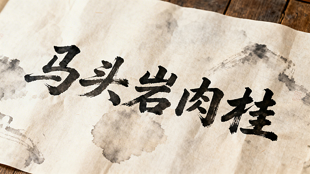 专业毛笔书法作品，内容为“马头岩肉桂”，采用古朴苍劲的毛笔字体，传统宣纸作为背景，带有自然的墨韵晕染效果，风格典雅大气，符合中式书法美学，整体画面简洁突出文字