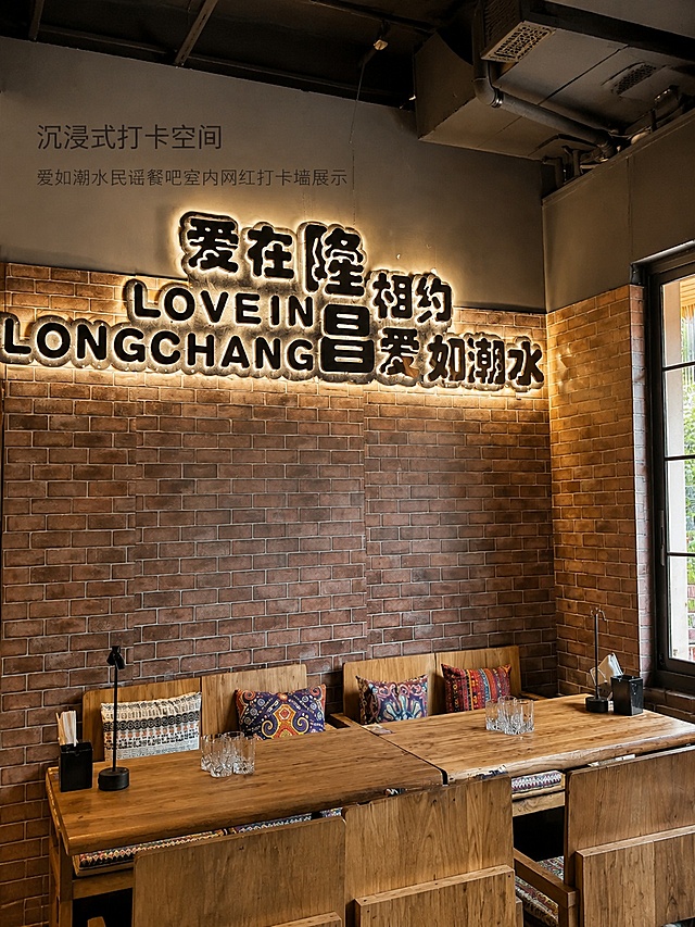 [第2屏] 门店环境展示，爱如潮水民谣餐吧室内网红打卡墙展示。本屏使用【图2】作为环境主体。
[氛围/风格] 真实门店氛围感，暖调自然光，复古工业风，保留红砖墙面原始质感。
[元素布局] 打卡文化墙占据画面中心区域，占比约70%；下方展示木质餐桌和彩色抱枕，突出门店休闲用餐环境，墙面文字和装饰保留原样，整体构图稳定自然。
[光影质感] 自然侧光照明，墙面砖块纹理清晰可见，桌面光线柔和，整体明暗过渡自然，保留真实环境质感。
[配色色系] 全局底色#e8e2d5；主色红砖墙棕色，搭配木色餐桌；辅助色彩色抱枕点缀。
[视角构图] 正面平视视角，景深适中，清晰展示墙面整体和下方用餐区，阅读动线自然从上到下。
[文字版式] 画面上方小标题「沉浸式打卡空间」，浅黑色小字左对齐，不遮挡主体墙面文字，保留原墙面「爱在隆昌 相约爱如潮水」文字清晰可见。
[比例分辨率] 3:4竖版比例，4K分辨率，文字清晰可辨，高清画质。
[负向提示词] 墙面变形，文字模糊，颜色偏差，杂物遮挡，曝光过度。