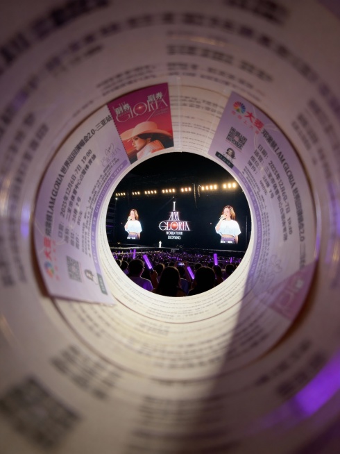 把图1的演唱会门票卷成隧道形状，通过圆形洞口呈现透视效果，强纵深感。隧道尽头展示图2的演唱会现场场景。固定聚焦在演唱会场景上，周围呈现朦胧模糊、拖影的效果。预览效果
