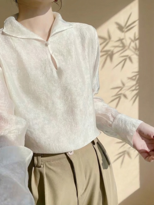 参考原图，保持图中模特姿态不变，保持这件衬衫的版型、花色、颜色、面料纹理、纽扣细节完全不变，只更换背景。背景改为暖色系新中式极简风氛围，自然侧光，窗外竹影投射在暖米色墙面上，大面积留白，静谧禅意，商业预览效果