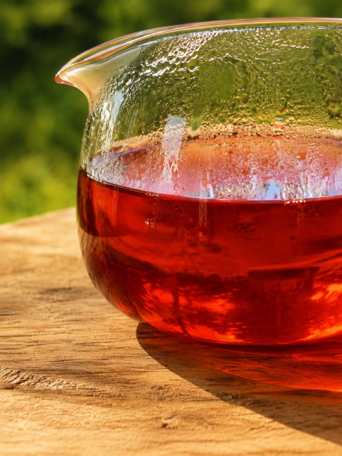 保留现有茶汤特写内容，将图片比例修改为3:4，保持侧逆光通透感，诱人红棕色茶汤，玻璃公道杯和原木桌面，户外绿色背景不变，画质清晰。预览效果