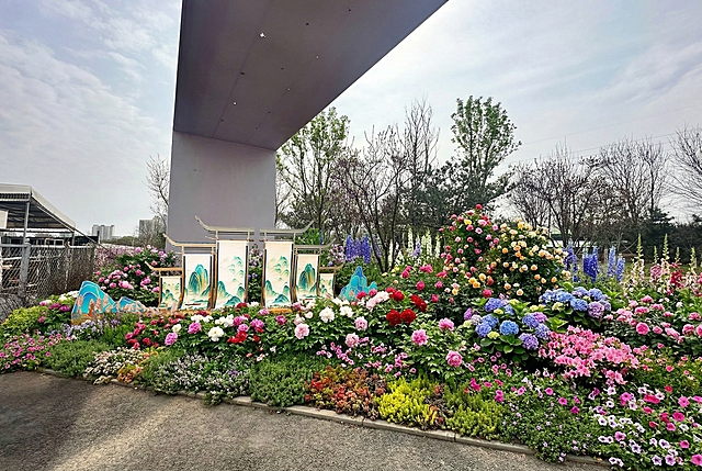 在现状场地基础上，打造立体花境，通过地被、主花、高杆植物三层搭配，形成前低后高、色彩丰富的迎宾花带。保留原有建筑与场地肌理，利用牡丹、月季、绣球、杜鹃、时令草花等营造繁花簇拥效果，实现开门见花、四季有景，整体氛围热烈雅致、层次饱满，完美呈现“百花迎门”的视觉与意境。保留图片中原有的中式山水装饰装置