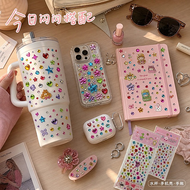 第5张 多场景应用主图｜加州少女DIY桌面
1:1正方形商品主图，加州阳光美式ins风，暖调自然光+补光，浅木色桌面，整体松弛生活化，种草感强。
画面桌面随性摆放日常物件：白色大容量冰霸杯、透明手机壳、粉色手账本、发夹、耳机壳，物件表面均粘贴同款彩色钻石贴纸，贴纸贴合平整，钻面高亮通透，明度拉满，切面反光自然，与包装钻面质感完全统一，真实呈现DIY装饰效果。画面右下角错落摆放两款原图钻石贴纸包装，作为产品露出，占比适中不抢场景主体。桌面点缀银色耳环、粉色甲油瓶、复古墨镜、白色耳机等美式少女小物，构图松散随性，像真实桌面分享。可局部露出少女手部拿取水杯，增加真实感。
画面顶部偏左用手写感标题标注「今日闪闪搭配」，白字浅粉描边；右下角配迷你标签「水杯·手机壳·手账」，透明底白字，融入场景不突兀。