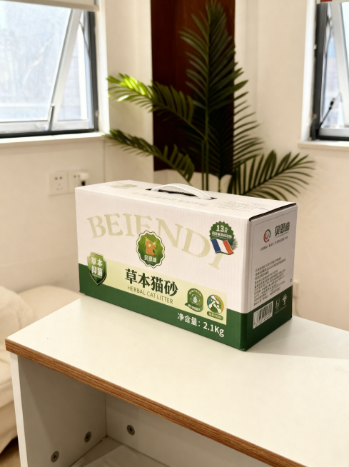 贝恩迪草本猫砂包装盒，白绿配色纸盒包装，带手提结构，保持产品原有文字、Logo和包装信息不变，严禁扭曲变形。生成参考图同款简约温馨室内家居场景，使用全屋漫射柔光，低对比度，淡柔和阴影，画面明亮干净。采预览效果