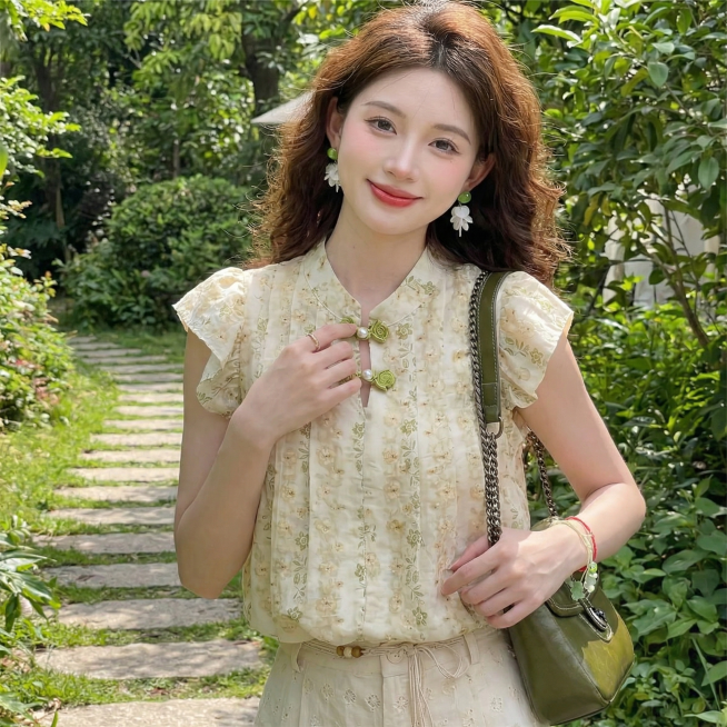 保留这件新中式改良旗袍上衣的款式、绿色刺绣盘扣和碎花细节全部不变，更换和上一张不同的模特姿势和清新户外背景，生成正方形1:1比例的全新原创淘宝女装主图预览效果