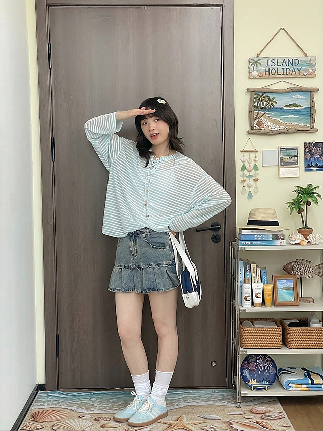 保持中心人物完全不变，按照要求优化环境部分：1. 地毯更换为带有夏日海滩贝壳元素的款式花纹；2. 优化侧面置物架柜子内的物品摆放，整理得更整洁并融入环岛假日主题元素；3. 在墙面添加适当的夏日海岛风格装饰，主题为环岛假日，融入夏天、小岛、海岸线、贝壳、烟火、椰子树的氛围元素