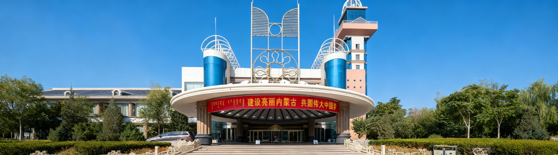 将这张酒店大门图片整体压缩适配到360*100像素画布，保留完整圆形门楼、装饰雕塑和横幅文字，横版构图，保持原有清晰画质和晴朗蓝天实景氛围预览效果