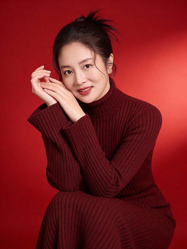 暖调红背景衬托深红针织套装，柔光勾勒优雅轮廓，面料质感细腻，传递温馨与舒适，尽显时尚与柔和之美。换个动作
