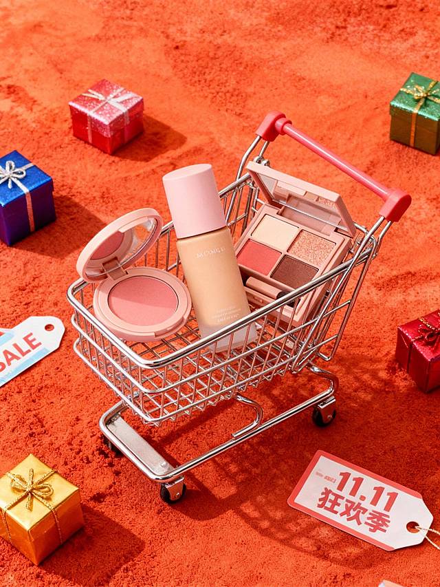 以红橘细腻粉末纹理为背景，中央是银色购物车，图内商品被装入购物车内，周围散落彩色礼盒、写着"SALE"、“11.11 狂欢季”的促销标签，整体营造购物氛围。