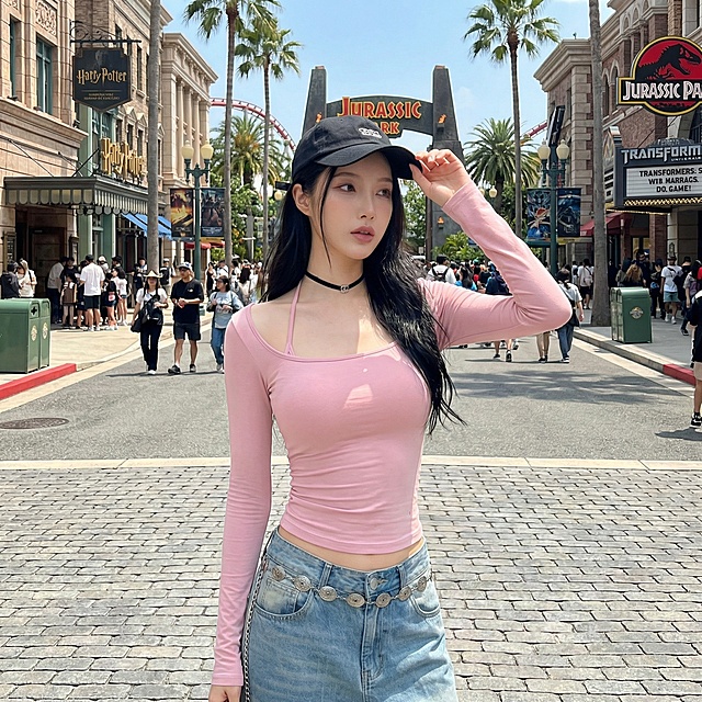 将背景替换为环球影城内部场景，保持模特和衣服不变，更换为单手扶帽的姿势