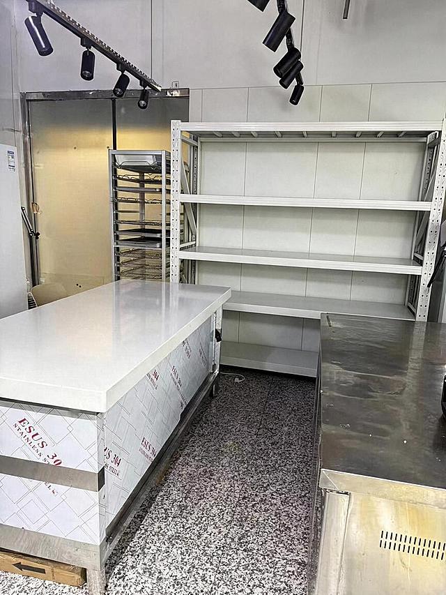 去除后方白色货架右上角被透明塑料袋包裹的风扇设备，去除后用周围真实的白色墙面和货架顶部结构自然填充，光影和材质与原图完全一致，过渡自然无痕。严格保持图片中其他所有主体、物品、细节、结构、颜色、光线、透视角度完全不变，不得添加或修改任何其他元素。最后整体提升图片清晰度，画质自然真实，保持原照片的真实感。