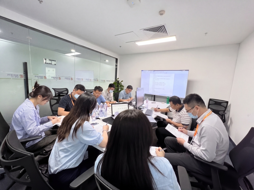 保留原图环境和物品陈列，保持9个人物（3女6男）分坐会议桌两侧，全部人物低头答题，姿势自然，生成真实自然的员工参与网络安全考试现场照片，接近真实会议室环境预览效果