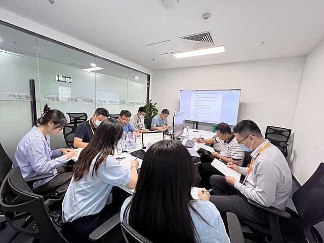 保留原图环境和物品陈列，保持9个人物（3女6男）分坐会议桌两侧，全部人物低头答题，姿势自然，生成真实自然的员工参与网络安全考试现场照片，接近真实会议室环境