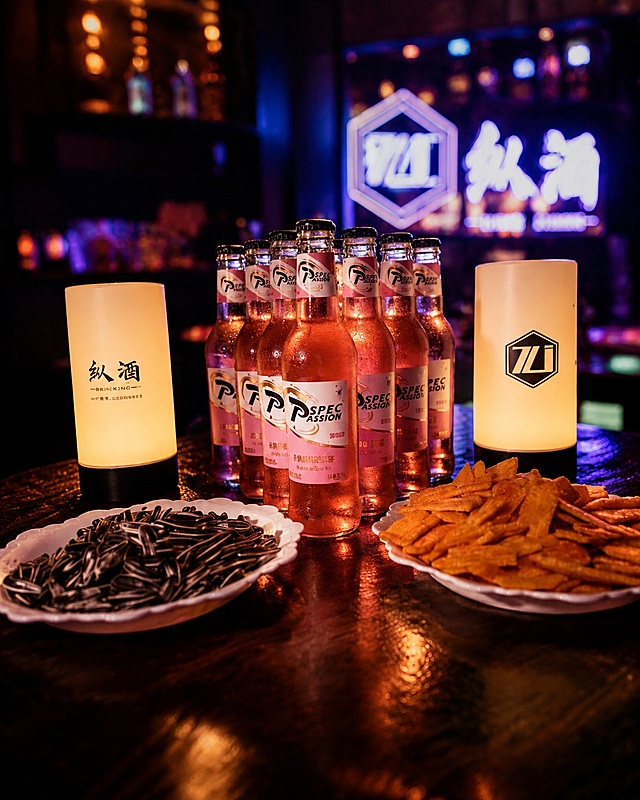 将这张清吧宣传图重绘为高级氛围感酒吧宣传大片，保留桌上的粉色果味啤酒瓶、两盏印有“纵酒”字样的暖光桌灯、瓜子和脆片小食，背景保留“纵酒”发光书法字招牌。整体升级为暗调轻奢清吧氛围，暖橙色灯光柔和打在酒瓶和小食上，瓶身有精致的水珠和通透的液体光泽，木质桌面有细腻的反光，背景虚化带霓虹光斑和微醺的蓝紫色调，电影感构图，质感高级，有让人想喝酒的微醺氛围感，商业摄影级别，高清细腻