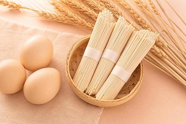 保留挂面、鸡蛋和麦穗真实的外观形态和细节质感，去除面纸上的红色文字，整体风格与之前的饼干图统一：马卡龙浅暖色系柔和渐变背景，温暖柔和的自然光效，画面干净明亮治愈可爱，突出食材的新鲜质感，构图精致美观，画面不加任何文字