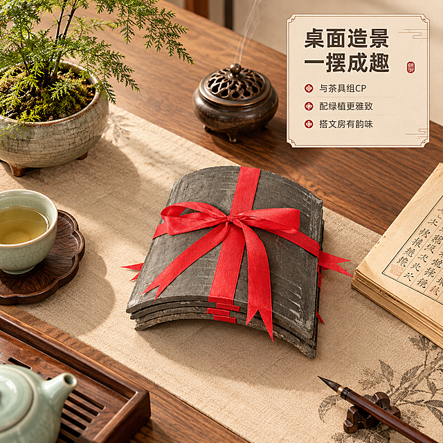 [商品] 使用【图1】【图5】瓦片捆红绳装饰摆件；保留瓦片弧形结构、青灰色材质、红绳十字捆绑蝴蝶结造型；商品处理：保留原有结构与颜色，增强瓦片肌理质感，去除原背景。
[画面] 目标为桌面造景搭配灵感展示。新中式书桌桌面场景，瓦片捆红绳摆件作为视觉焦点，周围搭配：青瓷茶杯、木质茶盘、小型文竹盆栽、线香炉、古籍书页。整体营造雅致文人桌面氛围，展示摆件如何融入桌面造景。俯拍角度，桌面占满画面。
[视觉] 套系策略：风格=新中式复古商业摄影；标题字=阿里巴巴普惠体粗体；正文字=阿里巴巴普惠体常规体；主色=青灰瓦色+暖米杏色；背景延展=基于暖米杏做深浅层级、同色渐变和宣纸/木质肌理质感；强调色=中国红，仅用于小面积图标、引线和标签点缀；标题色=深炭灰；正文色=中暖灰；组件=圆角浅底信息卡、细线引线、中式回纹装饰元素；光影=左前侧暖柔光，右侧柔和补光。
[文字] 右上角信息卡主标题「桌面造景 一摆成趣」，配3个搭配建议：与茶具组CP | 配绿植更雅致 | 搭文房有韵味。文字不遮挡主体。
[规格] 图片比例1:1，4K分辨率，避免变形、错字、文字过小、冷蓝背景、颜色改变、结构失真、极限词违规词。