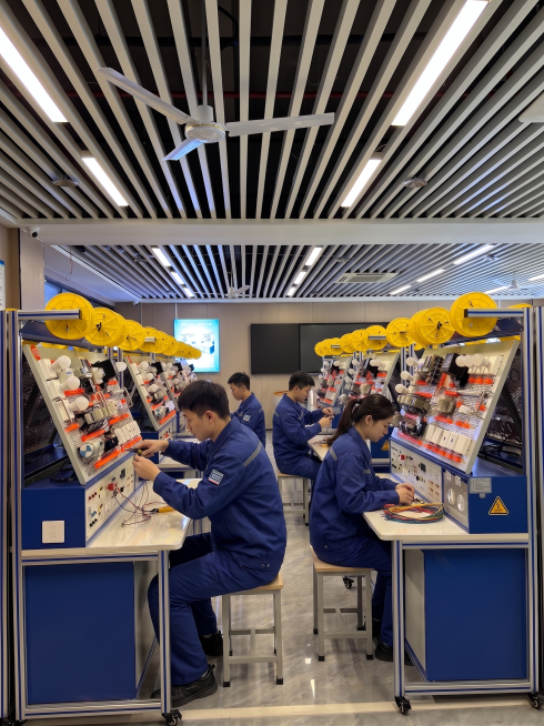 请保持参考图 1 中电工实训教室的整体场景、所有已存在的设施、前排电工学员都与原图一致，不做改动。在此基础上，在中后排设备的对应座位上，再添加2-3位穿着蓝色工装的电工学员，他们分别坐在各自座位前操作预览效果