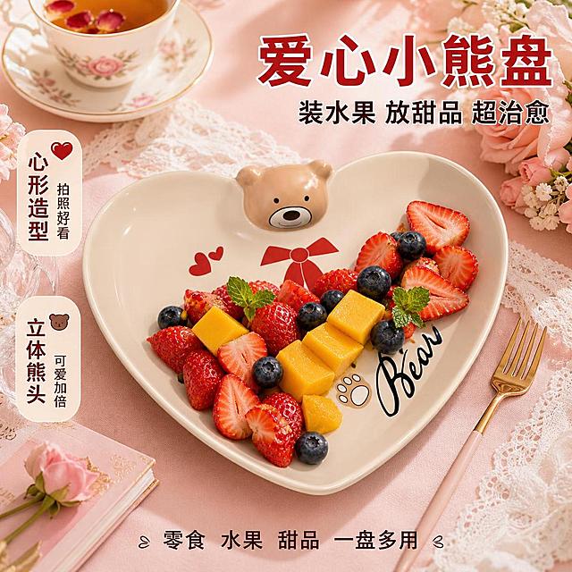 [主图-5] 爱心盘甜品水果场景图 少女心治愈风
[氛围风格] 甜美治愈 下午茶氛围 温馨浪漫
[画质] 超高清商业摄影 光线柔和 色彩温暖 产品真实
[元素] 画面主体为小熊头爱心盘，保持与输入产品图完全一致：奶咖米底色、心形造型、顶部立体小熊头、红色蝴蝶结、红色双爱心、Bear英文字样、熊掌印，杜绝变形色差。爱心盘中盛放切好的草莓、蓝莓、芒果块组成的水果拼盘，旁边放一把小叉子。背景是粉色系下午茶场景：浅粉色桌布、一杯花茶、一小束玫瑰花、蕾丝餐垫点缀。整体甜美治愈，突出爱心盘的可爱造型和甜品水果用途。商品主体占比约65%。
[光影] 柔和顶光+侧光，水果晶莹剔透，陶瓷盘釉面有细腻高光，整体温暖甜美。
[配色] 主色奶咖米白 辅色樱花粉 强调色草莓红
[视角构图] 俯视45°角，爱心盘为视觉中心，景深中等，周围道具丰富不抢主体。
[文字版式] 右上大字主标题"爱心小熊盘"红色粗体大号；副标题"装水果 放甜品 超治愈"中号深棕。左侧中部两个竖排小标签："心形造型""拍照超好看" 和 "立体熊头""可爱加倍"。底部小字"零食 水果 甜品 一盘多用"。
[输出要求] 1:1比例 文字清晰锐利 超高清商业摄影质感
[负向提示词] 变形 文字错乱 产品模糊 背景杂乱 水印 电商平台Logo 多余的手 畸形手