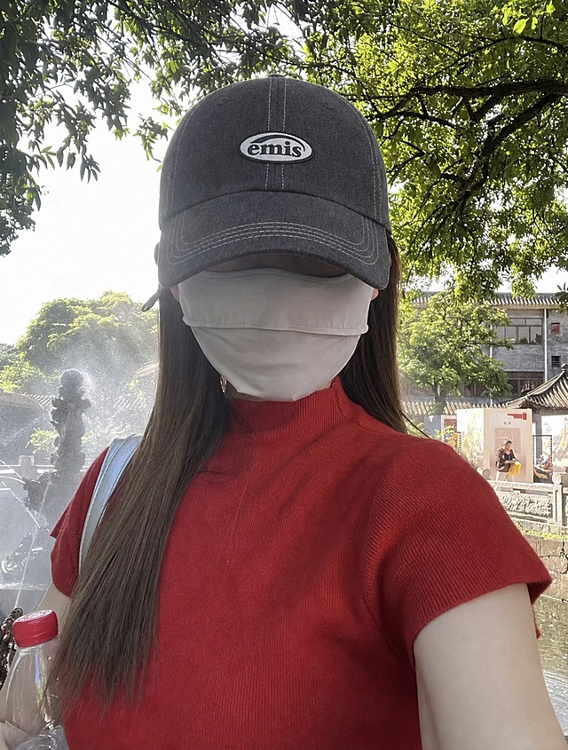 将图中人物头上的深蓝色帽子替换为图二中的深灰色emis棒球帽，保持帽子的佩戴角度、透视和光影与原图一致，自然贴合头部，其余人物、服装、背景和光线均保持不变，真实自然，无违和感