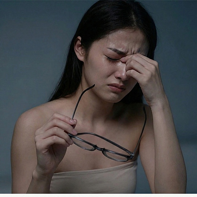 一位年轻女模特一只手拿着眼镜，另一只手揉着眉心，眉头紧锁、双眼紧闭，呈现疲惫烦躁的神情
