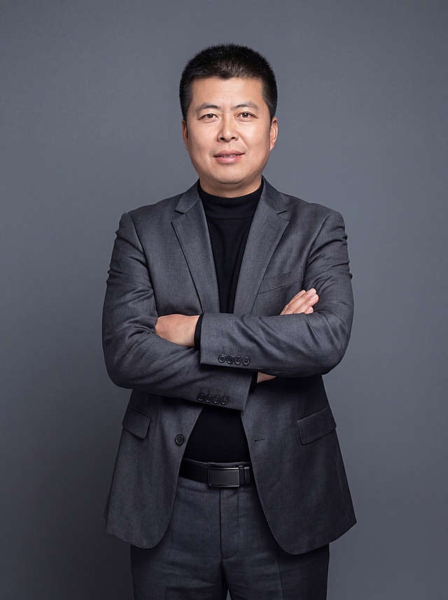 参考图中保留人物脸型、发型、年龄等特征生成职场形象照,标准焦段50mm,f/4光圈(f/2.8-f/4区间),平视视角(镜头与人物视线齐平);人物占画面70%,人物居中(居中构图),位于画面中心,为视觉聚焦点,入境范围头部及以下至臀部下方10cm(半身像);左右留少量背景空间;头部与画面顶部保留5%空间;头部发型完整,头肩比例协调,人物结构准确;发质微微柔顺，微微蓬松。身穿修身精纺羊毛混纺面料的深灰色西装外套(含5%桑蚕丝提升柔光质感),平驳领(商务感正式感),左胸袋无口袋巾(简化高级感),西装下摆自然垂度;内搭黑色中领紧身针织上衣,下装精纺羊毛混纺面料的深灰色高腰直筒西裤(面料同西装),搭配黑色哑光头层牛皮皮带(宽1.5cm),带扣为长方形拉丝黑色金属(1.8cm×2.5cm);着装正式干练;专业稳重;身形匀称,姿态端正,身体挺拔。呈正面抱胸的自然站立姿态:左臂搭于右臂上方,肩颈自然松弛下沉,姿态自信从容；画质超高分辨率、细节清晰,现代精致感风格;肤质精细化处理;眼神直视镜头,目光坚定且澄澈,表情自然。嘴角上扬;简约冷调深灰色纯色背景(呈现均匀柔和质感),背景光线均匀柔和,强化色彩对比的高级感。极简干净;肤质自然细腻,肤色健康均匀,皮肤状态清爽干净,保留真实皮肤细节｡正面柔光补光,4800K中性光,面部光比1:1.5｡中近景写实摄影,对焦清晰,面部雾面柔光,轻透裸肌感,高清保留皮肤细节;分辨率4K,去除人物之外的所有元素。严格按照图片内容生成。画面比例3:4