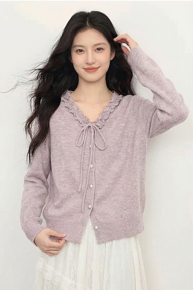 保持模特、淡紫色木耳边系带针织开衫、白色蕾丝半裙、纯白色背景、整体暖柔色调完全不变，仅更换姿势为：一只手轻轻抓着针织衫下摆，另一只手撩动头发，身体微侧，笑容柔和看向镜头，姿态自然，真实感强