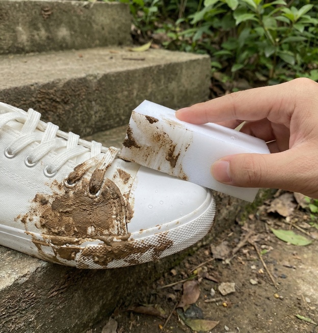 用图中的纳米海绵擦拭白色帆布鞋鞋头的泥土污渍，鞋头沾满褐色泥土，海绵擦拭后鞋头洁白干净，对比明显，场景为室外台阶旁预览效果