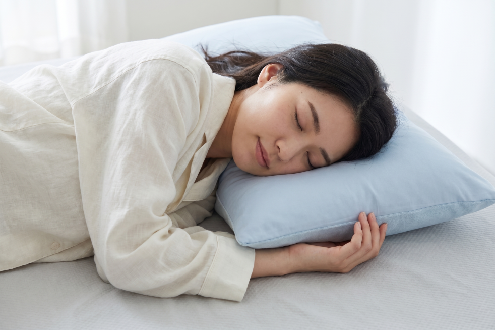 穿着米白色夏季家居服的日本青年女性，躺在床上枕着这款浅蓝色枕头睡得很舒服，特写商拍照片，给人凉爽舒适的感觉预览效果