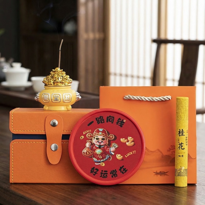 保留黄色聚宝盆香插、桂花线香、橙色礼盒皮箱、红色底座所有产品细节、包装文字和结构不变，更换为统一的新中式禅意茶室深色木质桌面背景，保持产品纹理、颜色不变，自然柔和侧光，氛围静谧雅致，商业静物摄影，1:预览效果