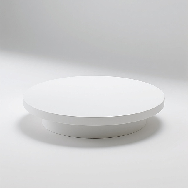 一张极简风格的白色圆形台面展示图，台面表面光滑平整，具有细腻的哑光质感，边缘线条圆润柔和。台面置于纯白色背景中，整体画面干净简洁，光线柔和均匀，从上方以45度角打光，在台面底部边缘形成淡淡的阴影，增强立体感。台面设计简约大气，没有任何多余装饰，配色仅有白色一种，营造出纯净、现代、高级的视觉氛围，适合作为产品展示的基础平台，信息传达直接高效，符合极简主义的设计美学。