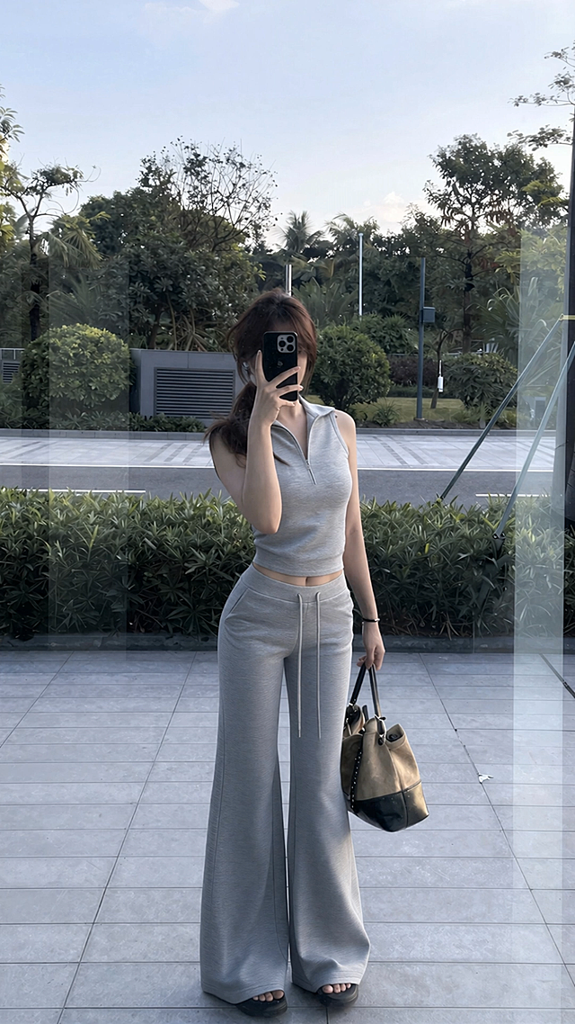 固定镜头，人物一只手举着手机对镜自拍，手机不要放下来，另一手拿着手提包并且往前走两步，微侧身又回正，动一下展示穿搭，动作流畅自然，整体自然真实，模特对镜自拍展示穿搭的过程，质感高级