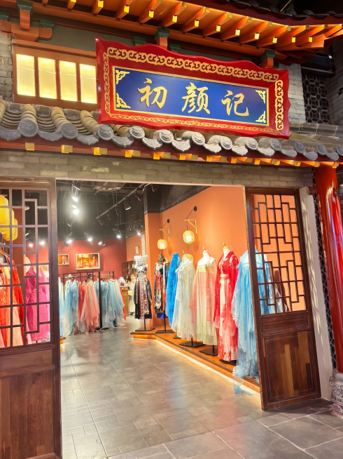 修改图片中的招牌文字，将原招牌的“国潮汉衣馆”替换为“初颜记”，保持招牌原有红底金纹蓝底金字的中式国风设计风格，字体为传统书法字体，整体协调美观，保持原图片其他内容不变预览效果