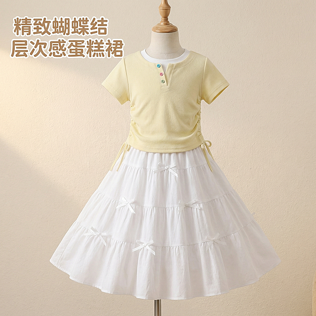 [垫图] https://gdesign-dam-hz.dancf.com/35968923572226148/fb8f67a431ce49b19018e2933d864597.jpg
[主图主题] 女童夏装套装细节展示主图
[氛围/风格] 小清新可爱风格，柔和室内摄影棚光线，清新干净
[画面元素] 重点展示白色蛋糕裙的蝴蝶结分层设计和细节，模特自然站立，裙摆撑开展示蛋糕裙层次，浅黄色短袖的彩色纽扣和侧边抽绳设计清晰呈现，背景为浅米色肌理墙面，背景简洁不抢主体，全屏无边框
[配色色系] 主色调：米黄+纯白，辅助色：浅米色背景
[视角构图] 中近景细节特写，聚焦产品核心设计，景深适中
[文字版式] 标题 "精致蝴蝶结 层次感蛋糕裙"，字体为圆润无衬线体，浅棕色，悬浮于画面左上角留白处，不遮挡产品细节，文字简约不突兀
分辨率 2K