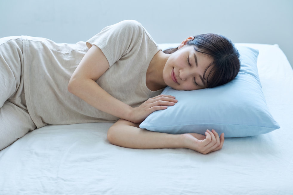 穿着米白色夏季家居服的日本青年女性，躺在床上枕着这款浅蓝色枕头睡得很舒服，特写商拍照片，给人凉爽舒适的感觉预览效果